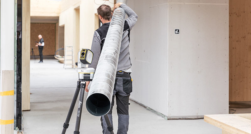 Leica iCON iCS50 motorised construction tool with construction worker carrying a large metal pipe.